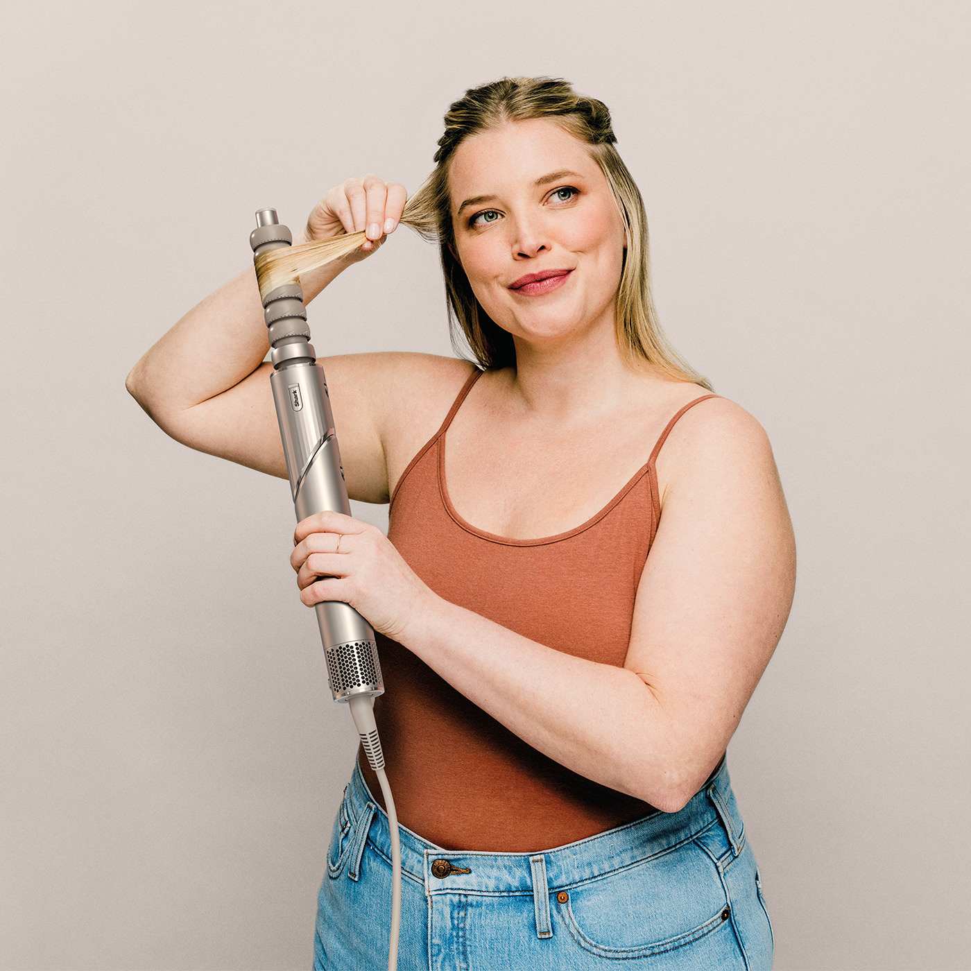 Woman styling her hair with a multi-styler curling attachment against a neutral backdrop.